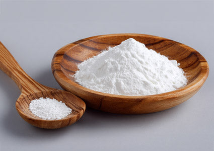 Acetyl L-Carnitine in wooden bowl and spoon filled with white powder on a gray background