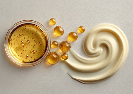Jar of gold-colored cream with droplets and a swirl of cream on a light gray background