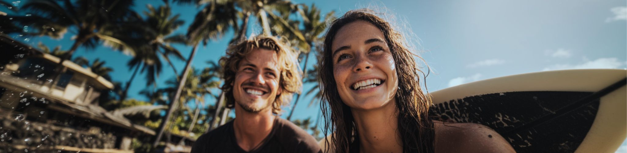 Two people with a surfboard, surrounded by palm trees and a clear sky